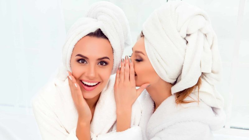 Girl in bathrobe and  towel on her head telling secret to her sister